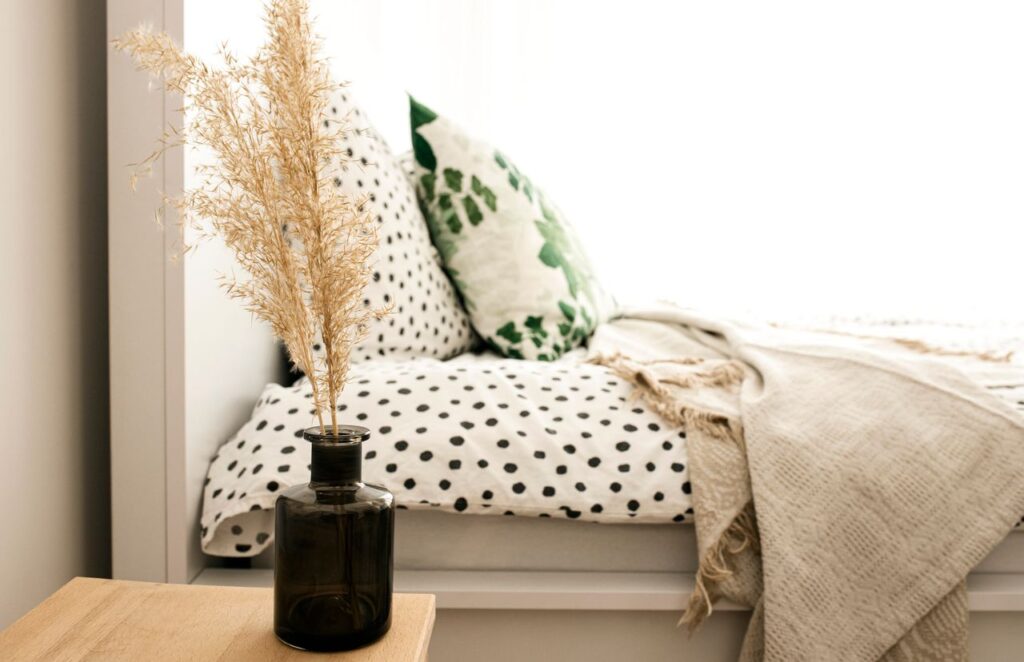 Cozy minimalist bedroom with polka dot bedding, wooden nightstand, and dried botanical arrangement for a Feng Shui layout