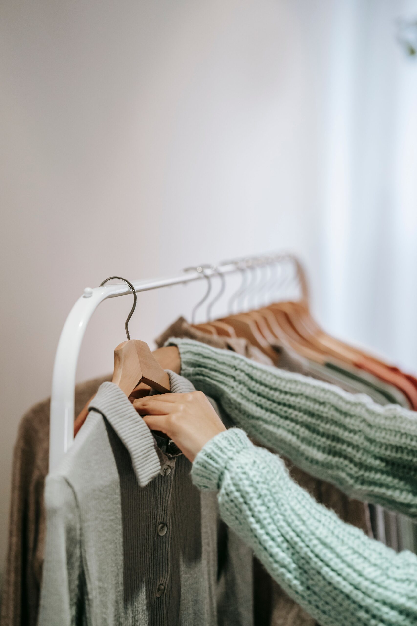 Organizing a minimalist capsule wardrobe with wooden hangers and neutral sweaters for CubeSmart self storage seasonal rotation.
