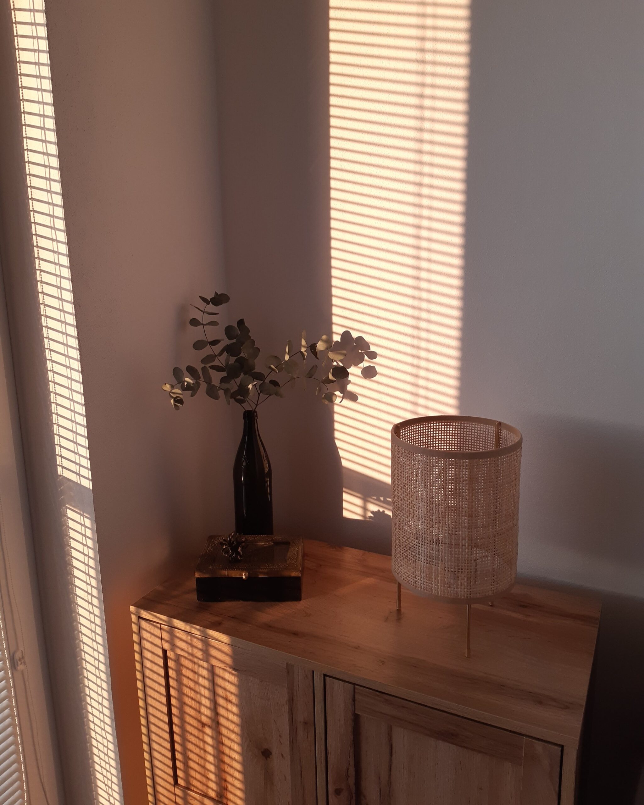 Serene minimalist home corner with warm wooden furniture, rattan lamp, and natural sunlight, highlighting the peaceful outcome of CubeSmart self storage.